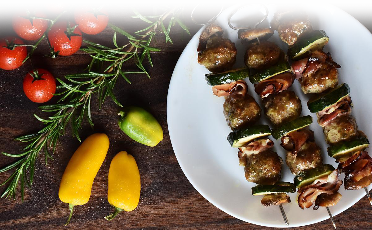 Tomatoes and peppers on a wood table with a plate of 3 chicken kabobs.