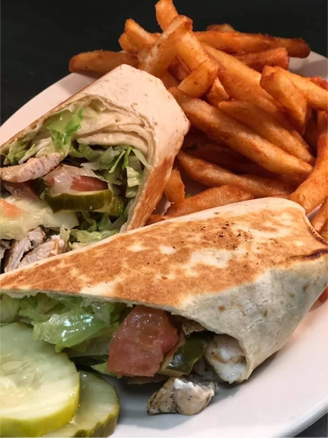 A plate with a sliced chicken Caesar wrap and french fries.